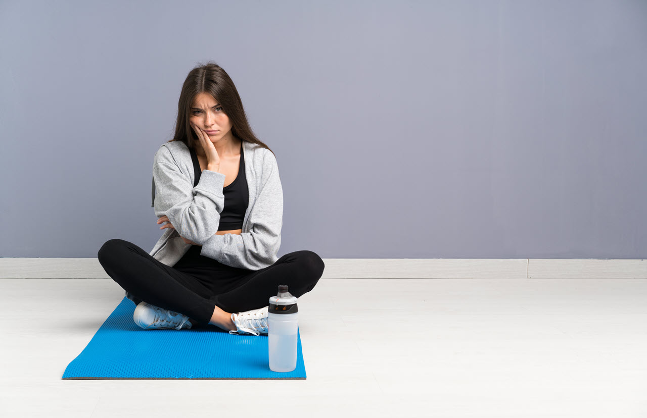 young-sport-woman-sitting-floor-with-mat-unhappy-frustrated